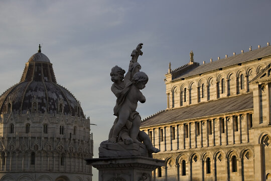View of the Fontana dei Putti statue with the Pisa Baptistery and Cathedral under a soft evening sky in Pisa, Tuscany, Italy.