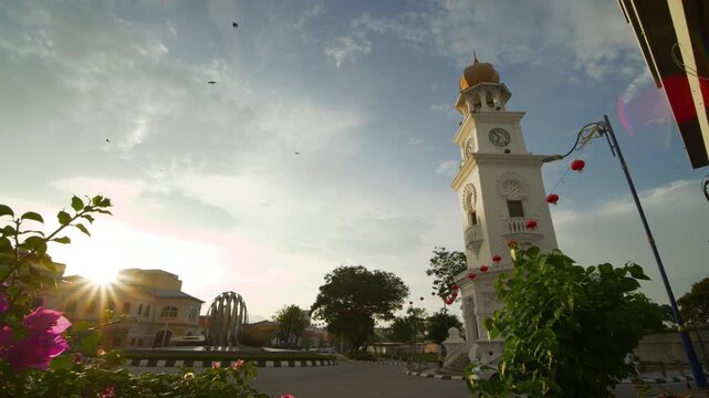 sunset time penang island george town city center clock tower front flowers view traffic street slow motion panorama 4k malaysia