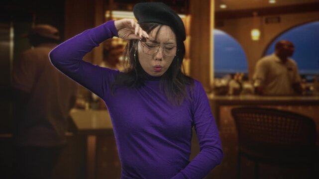 Woman in purple turtleneck and beret holds hand to forehead and squints, face visible with glasses near a bar counter and arched window sea view inside a building; tired contemplation.