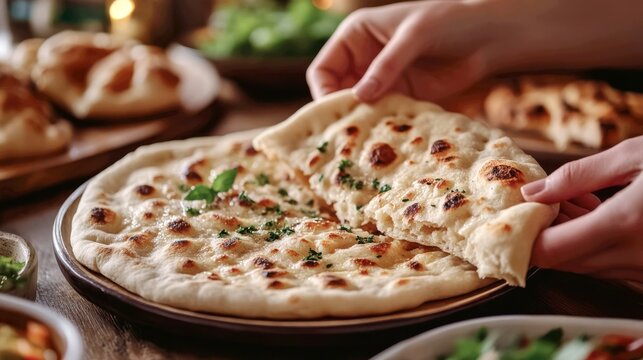 hands tearing a shared piece of lavash at a dining table. The focus is on the act of breaking bread together