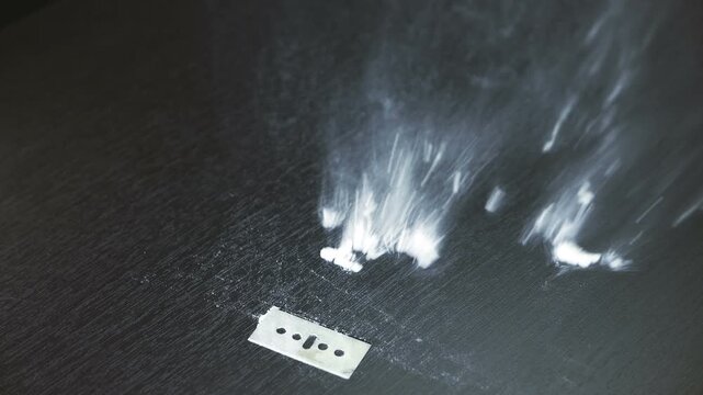 A line of cocaine or methamphetamine cut on a table next to a razor blade being blown away in slow motion. Addition treatment, quitting drugs.