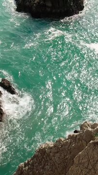 Aerial reveal of Dedo de Dios rock formation emerging above turquoise ocean waves near Maruata, Michoac&aacute;n.