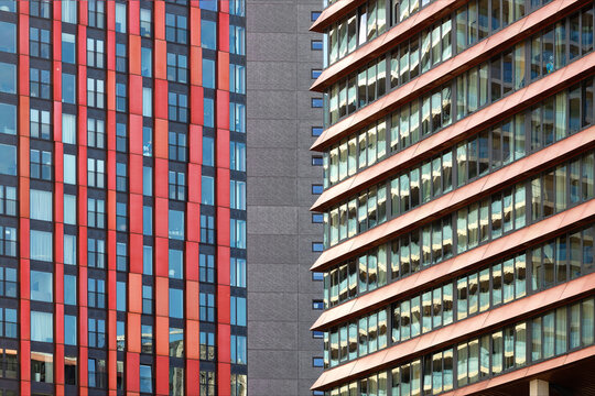 View of modern skyscraper facades with red vertical panels and glass windows featuring copper sunshades in the urban center of Rotterdam, South Holland, Netherlands.