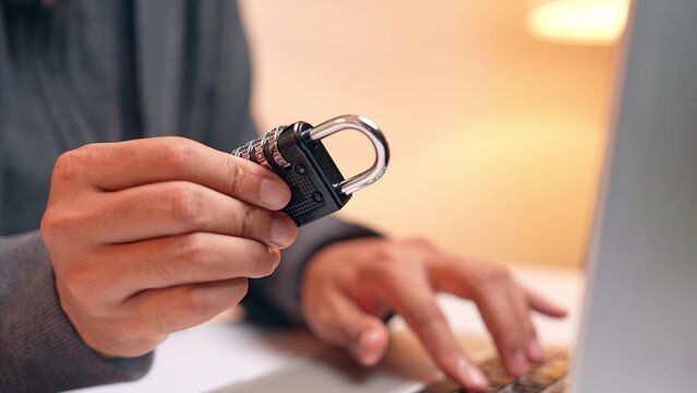 A hacker examines a padlock, symbolizing an attempt to crack security codes. This scene highlights digital vulnerability, data protection, password hacking, and the constant threat to cybersecurity.
