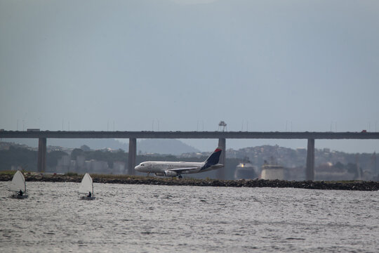 View of an airplane on the runway at Santos Dumont Airport with people in sailboats on Guanabara Bay and the Rio-Niteroi Bridge in Rio de Janeiro, Rio de Janeiro, Brazil.