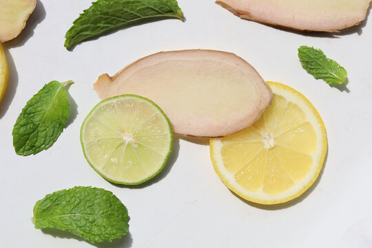 Fresh lemon and lime slices with raw ginger root pieces, and green mint leaves