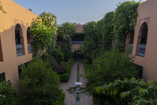 View of a traditional Moroccan courtyard with lush green climbing plants, arched windows, and a central water fountain in Agadir, Souss-Massa, Morocco.
