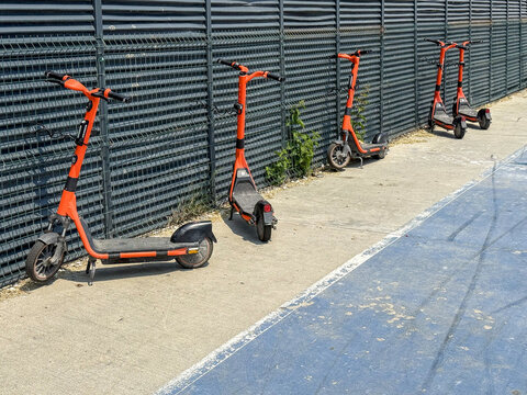 View of orange electric scooters parked in a row against a metal fence next to a blue bicycle lane on a sunny day Avcilar, Istanbul, Turkiye.