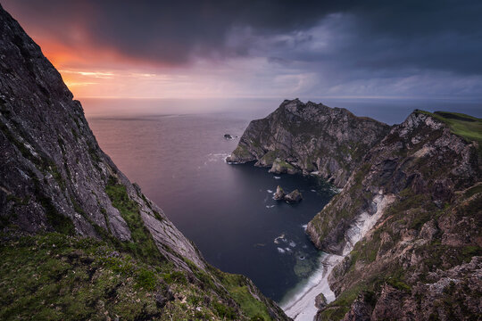 View of the Sturrall headland and steep sea cliffs under a dramatic sunset sky with dark clouds and the Atlantic Ocean in County Donegal, Ireland.