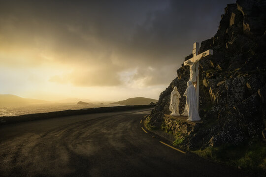 View of the crucifixion monument along Slea Head Drive overlooking the Atlantic Ocean during a dramatic golden hour sunset with dark clouds County Kerry, Ireland.