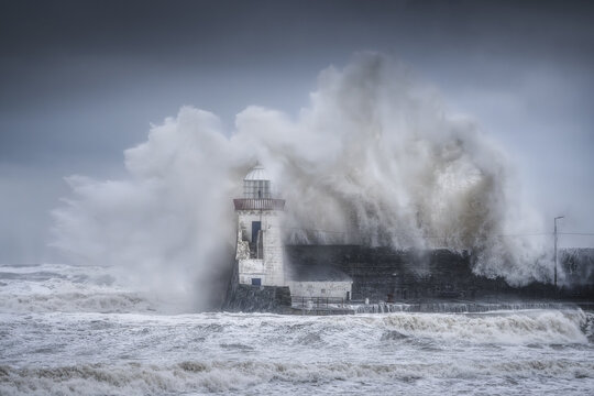 View of Balbriggan Lighthouse with massive waves crashing over the stone pier during a powerful storm under a dark overcast sky in Balbriggan, County Dublin, Ireland.