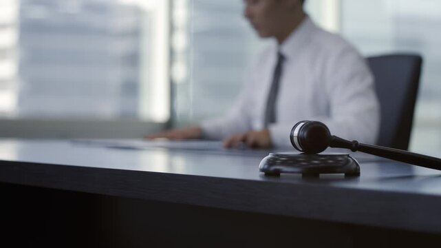 Gavel on a dark table with blurred business professionals shaking hands in the background, symbolizing legal agreement, justice, negotiation, and a successful deal.