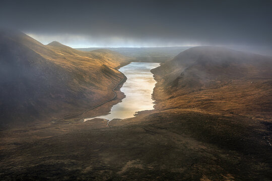 View of Silent Valley Reservoir nestled in the rugged Mourne Mountains with dramatic mist and golden sunlight reflecting on the water Newry, Northern Ireland, United Kingdom.
