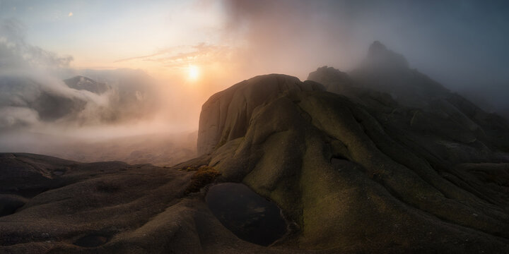 View of Slieve Binnian with dramatic rocky peaks and thick mist rolling over the slopes during a golden sunset in Newry, Northern Ireland, United Kingdom.