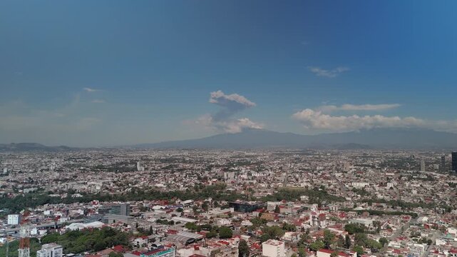 Scenic view of Puebla City with the majestic Popocat&eacute;petl Volcano rising in the distance and releasing volcanic smoke. A visually compelling Mexican landscape that combines urban architecture, natural