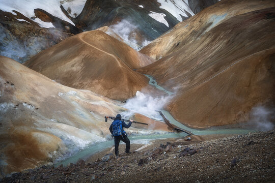 View of a photographer overlooking the steaming vents and colorful rhyolite mountains of Kerlingarfjoll with a turquoise stream Hrunamannahreppur, Iceland.