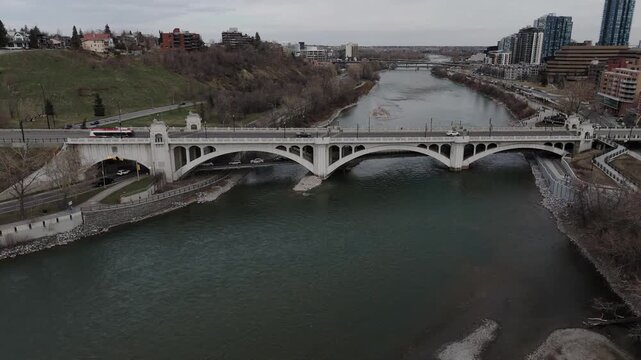 Cinematic fly-down aerial footage of Centre Street Bridge spanning the Bow River in Calgary, Alberta, Canada. The descending drone perspective showcases the historic bridge, flowing river, urban infra