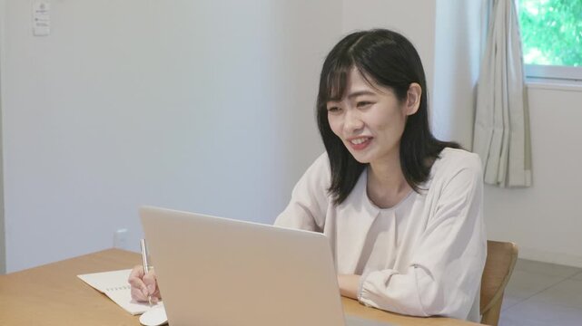 Young asian woman taking notes in notebook while working on laptop