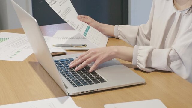 Close-up of woman's hands holding business document while working on laptop