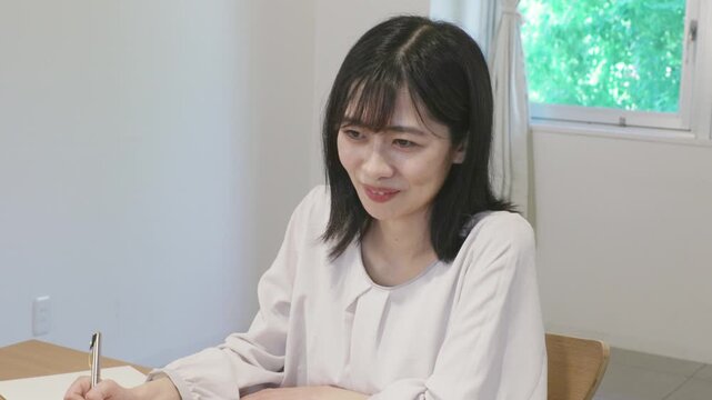 Young asian woman taking notes in notebook while working on laptop