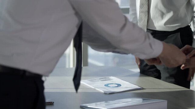 Businessmen in formal attire review financial documents with a pie chart on a modern office table, symbolizing collaboration, strategy, and corporate discussion.