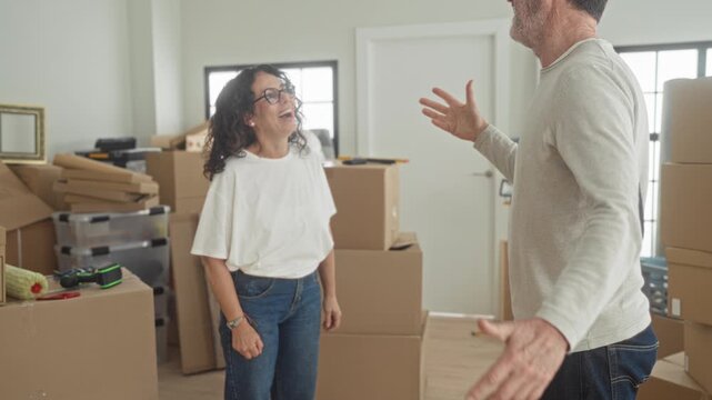 Woman returns fist bump to man amid stacked moving boxes and plastic storage crates in building during home relocation, both smiling; playful teamwork.
