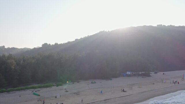 Pan view of people enjoying beach waves with hills and scenic coastal surroundings