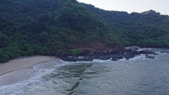 Dolly view of people enjoying beach waves with hills and scenic coastal surroundings