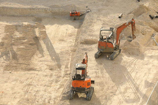 Orange Doosan compact track mini excavators operating on a sandy excavation construction site, preparing the ground for foundations.