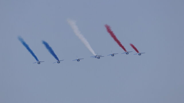 View of Patrouille de France aerobatic jets flying in formation leaving blue, white, and red smoke trails against a clear sky in La Ferte-Alais, Ile-de-France, France.