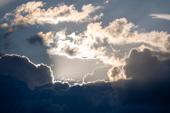 Silhouette of a commercial airplane flying through a dramatic gap in dark stormy clouds with glowing sunbeams and silver linings