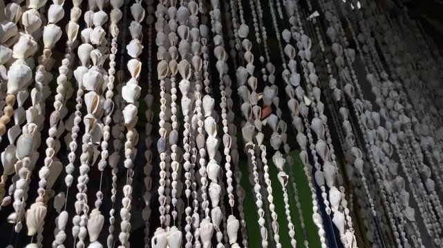 4k video footage of a curtain made from strings of seashells and sea snail shells hangs indoors as a decorative room divider.
