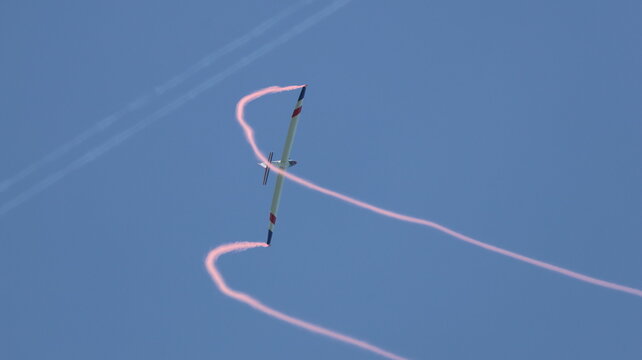View of a glider performing aerobatics with pink smoke trails against a clear blue sky in La Ferte-Alais, Ile-de-France, France.