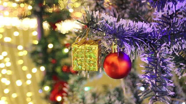 close up of a christmas tree decorated with a small golden gift box and shiny red ball. pretty holiday background