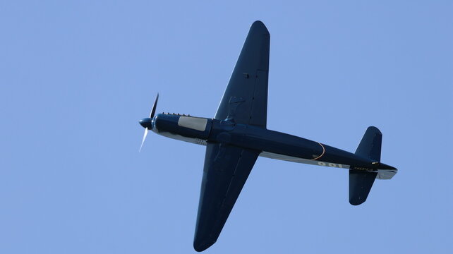 View of a vintage propeller plane performing a flight maneuver against a clear blue sky during an airshow in La Ferte-Alais, Ile-de-France, France.