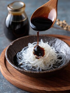 Transparent arrowroot noodles with black sugar syrup served in a dark bowl on a wooden table.