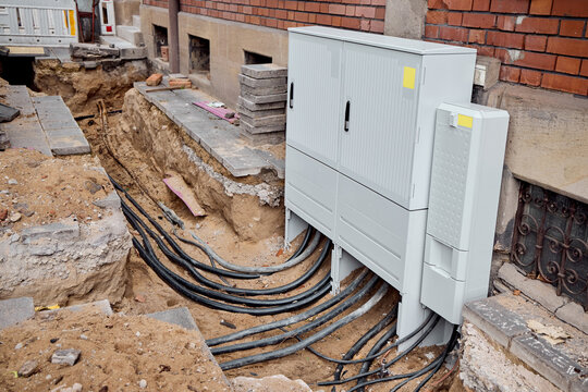 Outdoor street cabinet connected to underground fiber optic internet and power utility cables at an urban construction site.