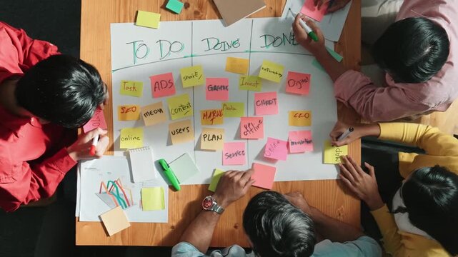 Top view of people writing and making scrum task board while writing marketing and planning strategy at colorful sticky notes. Smart team manage work performance by using kanaban board. Convocation.