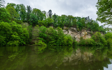 Obraz premium Panoramic view of sandstone rocks in Cesky Raj (Bohemian Paradise), rising above a calm pond in spring. Trees grow from rocky cliffs, reflected in the still water below.
