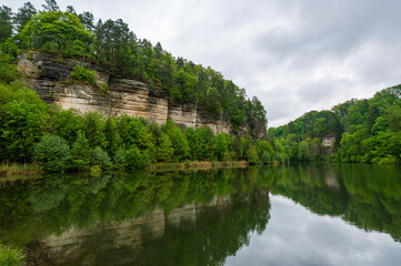 Fototapeta premium Panoramic view of sandstone rocks in Cesky Raj (Bohemian Paradise), rising above a calm pond in spring. Trees grow from rocky cliffs, reflected in the still water below.
