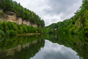 Obraz premium Panoramic view of sandstone rocks in Cesky Raj (Bohemian Paradise), rising above a calm pond in spring. Trees grow from rocky cliffs, reflected in the still water below.