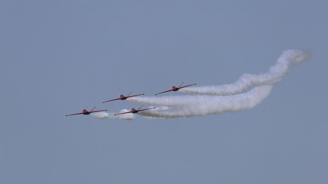 View of four red aerobatic jet planes flying in formation and leaving white smoke trails against a clear blue sky during an airshow La Ferte-Alais, Ile-de-France, France.