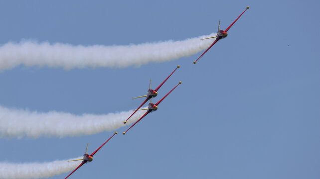 View of four red aerobatic planes performing a formation flight with white smoke trails against a clear blue sky La Ferte-Alais, Ile-de-France, France.