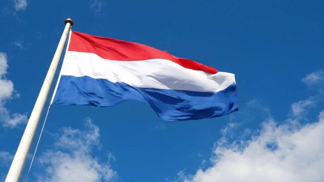 Dutch flag waving on a flagpole against a blue sky with clouds