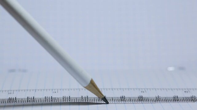 A student draws with a pencil under a ruler in a notebook at school