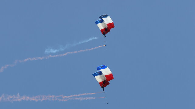 View of parachutists descending with French flag colored parachutes and leaving smoke trails against a clear blue sky during an air show in La Ferte-Alais, Ile-de-France, France.