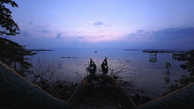 Twin naga statues framing calm sea with distant horizon at dusk