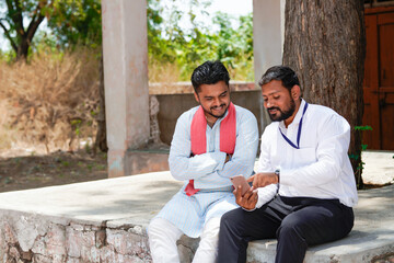 Obraz premium Indian banker or agronomist showing some detail in smartphone to farmer