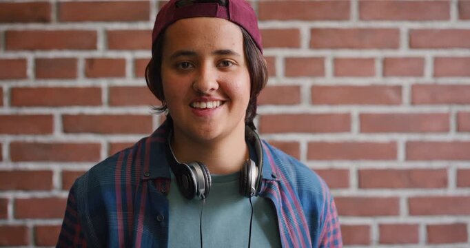 Face, laugh and student by brick wall with headphones for music education or future development. Portrait, teenager and funny boy with audio tech for academic podcast, scholarship and background