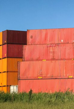 View of stacked red and orange shipping containers in a grassy field under a clear blue sky in Avcilar, Istanbul, Turkiye.